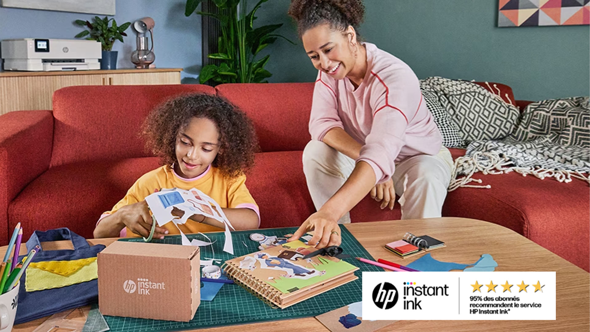 Bambina e donna creano lavoretti su un tavolo con materiali artistici, sedute su un divano rosso. Sullo sfondo, un mobile e una pianta.