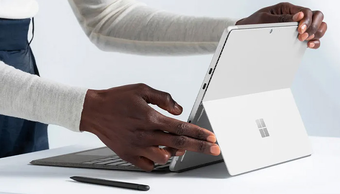 Una persona regola un tablet grigio con una tastiera grigia e una penna nera su un tavolo bianco.