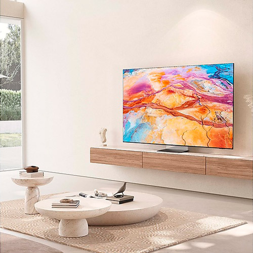 Soggiorno luminoso con TV a schermo piatto sopra un mobile in legno, tavolini bianchi e tappeto beige.