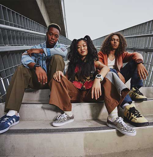 Tre persone siedono su gradini di cemento con ringhiere metalliche. Indossano abiti casual e scarpe da ginnastica.