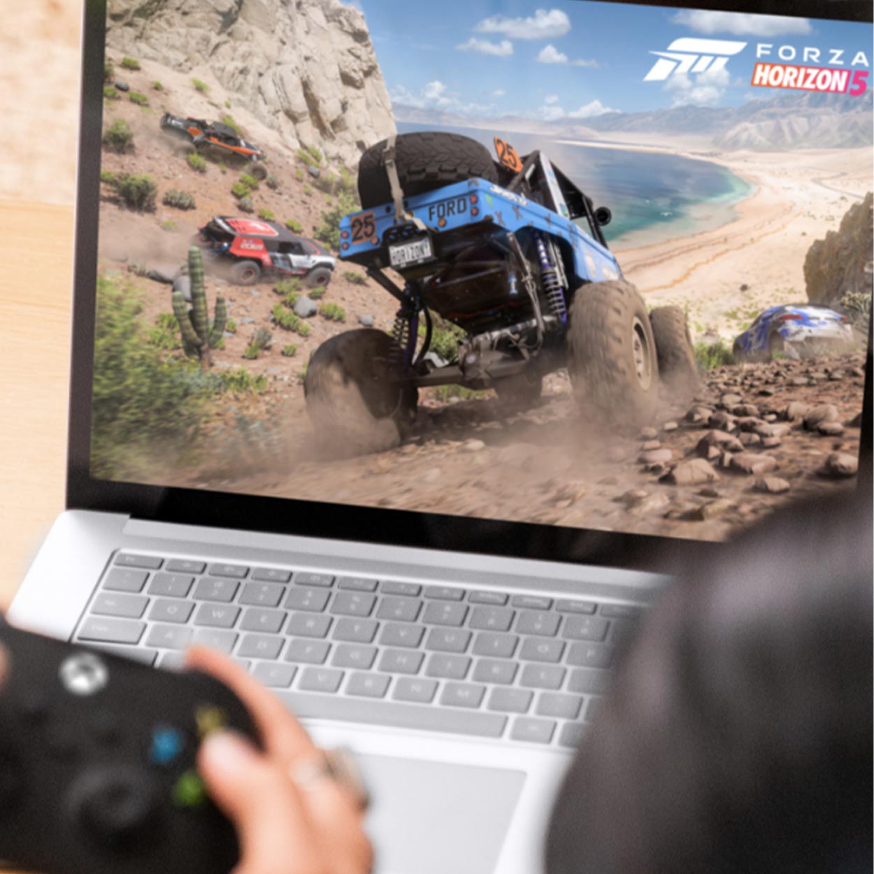 Videogioco Forza Horizon 5 su laptop. In primo piano, mani che tengono un controller Xbox. Sullo schermo, fuoristrada su un terreno roccioso.