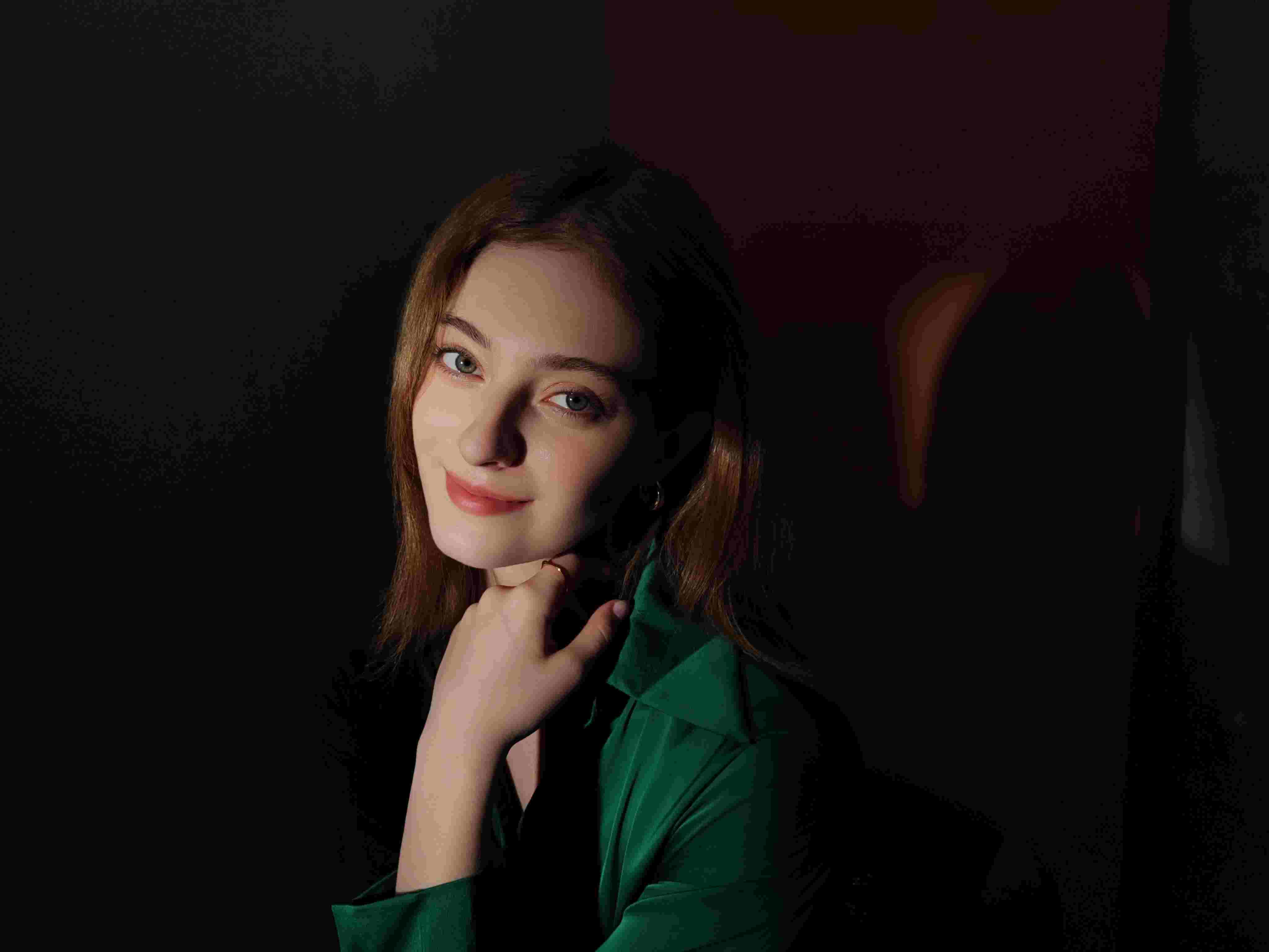 Donna con camicia verde, mano al mento, sfondo scuro.