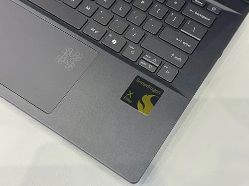 Dettaglio di un laptop grigio con tastiera nera e touchpad. Adesivo "Snapdragon X Elite" visibile.