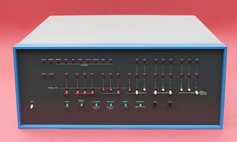 Un computer vintage con luci rosse, interruttori bianchi e scritte su un pannello nero, incorniciato in blu.