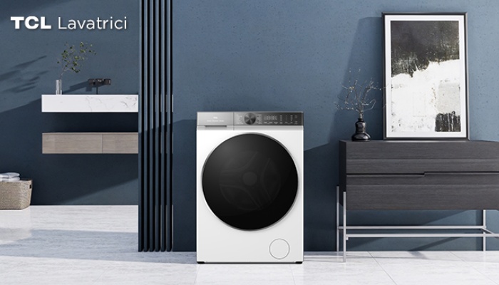 Una lavatrice TCL bianca con un grande oblò nero e pannello di controllo scuro, posizionata in un bagno moderno con pareti blu e mobili minimalisti.