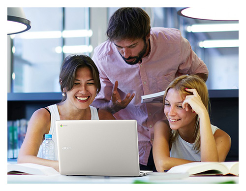 Tre persone attorno a un laptop su un tavolo con libri. Un uomo in piedi, due donne sedute. Bottiglia d'acqua sul tavolo.