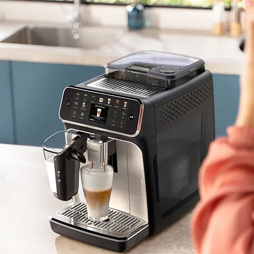 Macchina da caff� automatica nera e argento su un ripiano. Un bicchiere contiene una bevanda a strati. Lavello sullo sfondo.