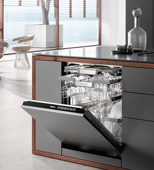 Cucina moderna con lavastoviglie aperta, piena di piatti. Finestra sullo sfondo con vista mare.