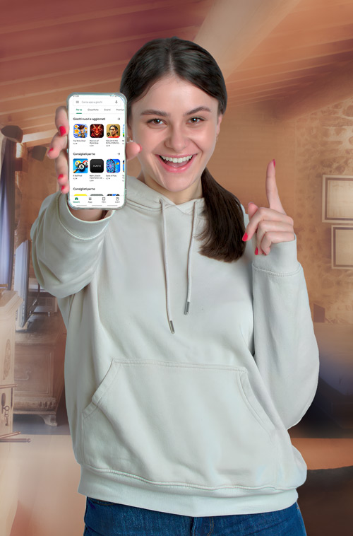 Donna sorridente mostra uno smartphone con app, indossa felpa grigia e jeans blu. Dietro, parete marrone con quadri.