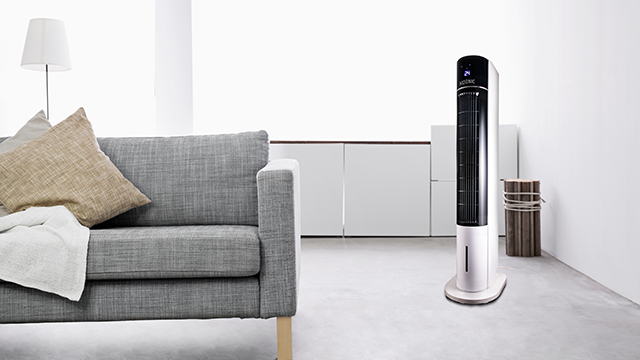 KTFC 603022 Il ventilatore a torre di KOENIC &egrave; posizionato in un soggiorno moderno e luminoso accanto a un divano grigio.