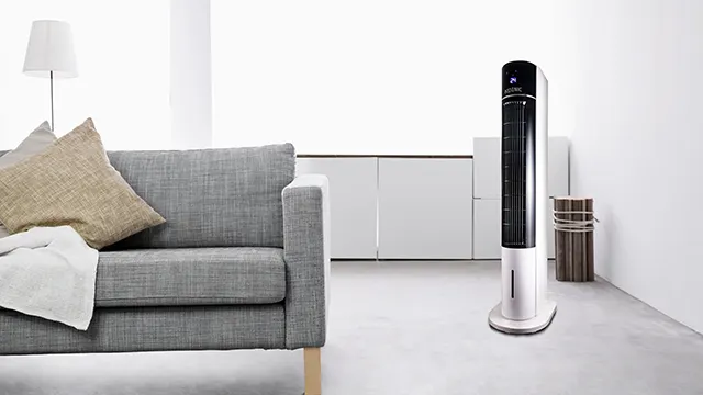 KTFC 603022 Il ventilatore a torre di KOENIC è posizionato in un soggiorno moderno e luminoso accanto a un divano grigio.