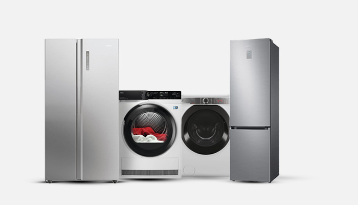 Due frigoriferi grigi affiancati a due asciugatrici bianche con oblò nero. Sullo sfondo bianco.