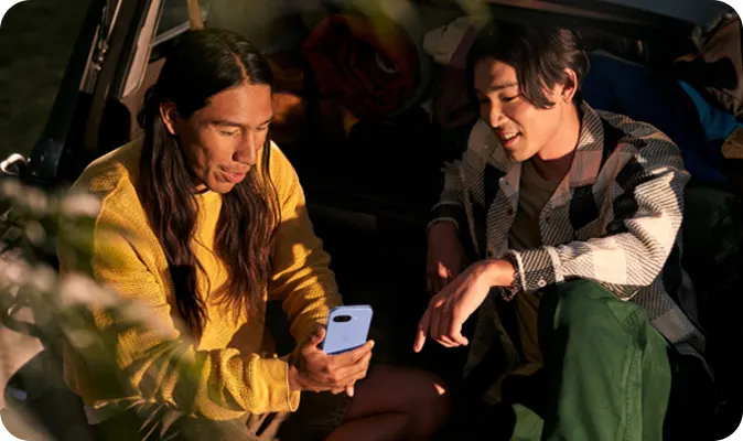 Due persone sedute in tenda guardano un telefono blu. Uno indossa una felpa gialla e l'altro una camicia a quadri.