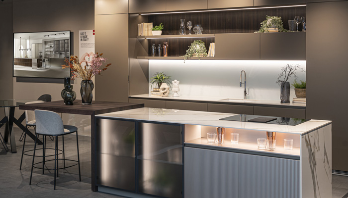 Cucina moderna con isola centrale, ripiani illuminati e tavolo da pranzo. Vasi con fiori e sedie alte completano l'arredamento.