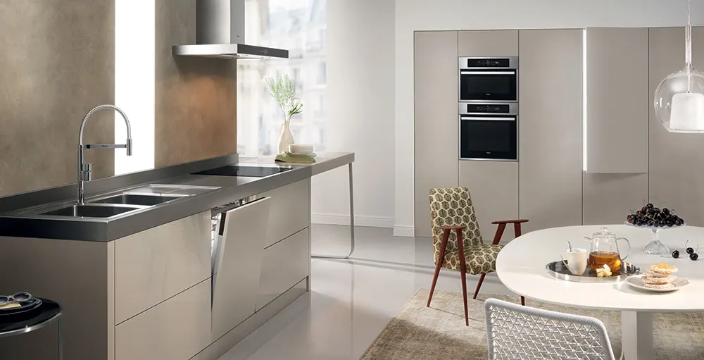Cucina moderna con lavello in acciaio, piano cottura, forno a muro e tavolo rotondo con cibo e bevande.