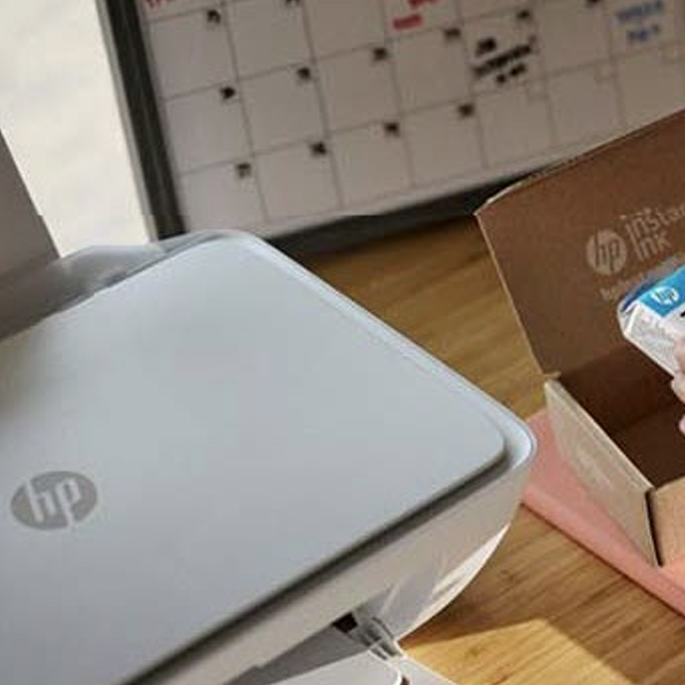 Stampante bianca, cartuccia d'inchiostro in scatola marrone, calendario a muro con griglia.