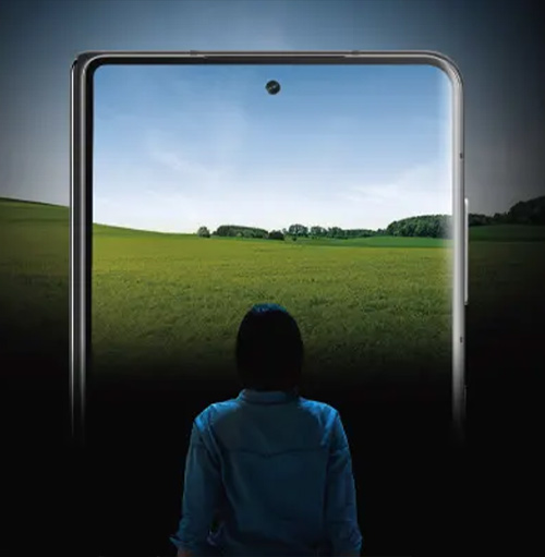 Una persona guarda uno smartphone che mostra un campo verde sotto un cielo azzurro.