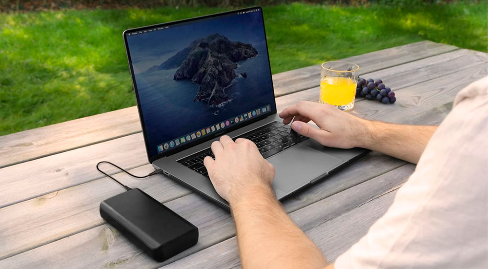 Persona usa un laptop su tavolo di legno. Sul tavolo ci sono succo d'arancia e uva. Un hard disk esterno � collegato al laptop.