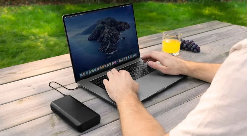 Persona usa un laptop su tavolo di legno. Sul tavolo ci sono succo d'arancia e uva. Un hard disk esterno � collegato al laptop.