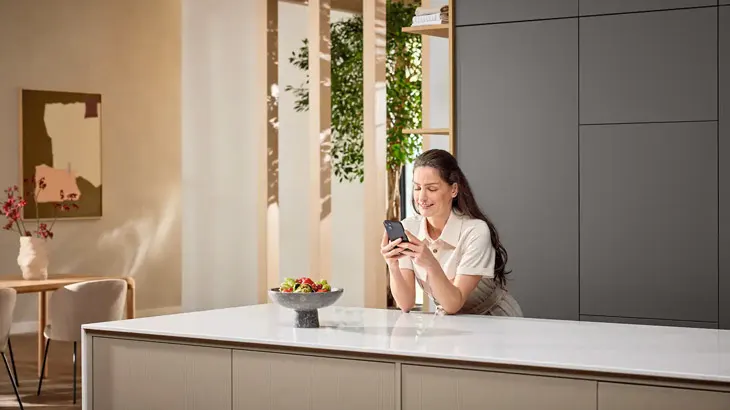 Una donna appoggiata in cucina mentre guarda lo smartphone