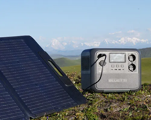 Pannello solare nero inclinato su un prato, con generatore d'energia portatile grigio. Montagne sullo sfondo.