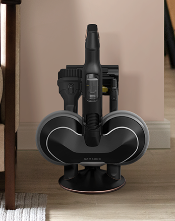 Aspirapolvere verticale nera su base di ricarica, su pavimento di legno. Sfondo: parete beige. Tappeto bianco e mobile marrone a lato.