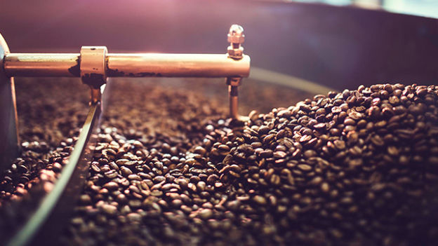 Primo piano di chicchi di caff� tostati in una torrefattrice con parti metalliche visibili.