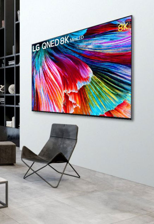 Soggiorno con TV LG QNED 8K con schermo multicolore e poltrona nera su pavimento grigio. Libreria a muro sullo sfondo.