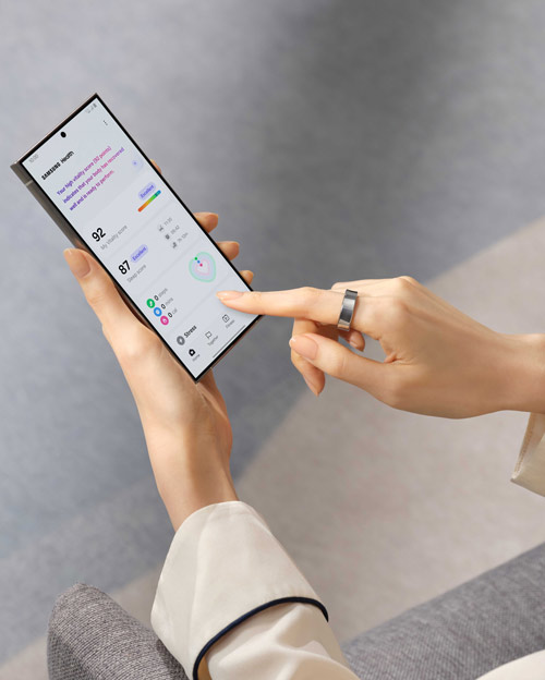 Mano che tiene un telefono con schermo dati. Un dito con anello tocca lo schermo. Sfondo grigio chiaro.