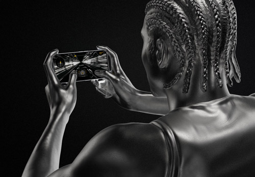 Statua in metallo di persona che tiene un telefono orizzontalmente con una strada visualizzata. Lo sfondo è nero.