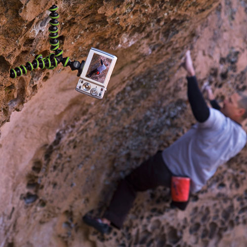 Un uomo scala una parete rocciosa. Una fotocamera su un treppiede registra l'arrampicata. Sullo sfondo, roccia.