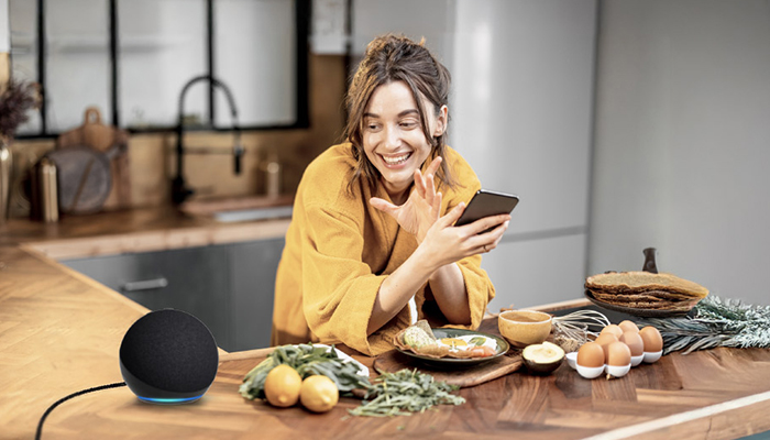 Donna sorride guardando il telefono in cucina. Un dispositivo intelligente, cibo e uova sono sul bancone.