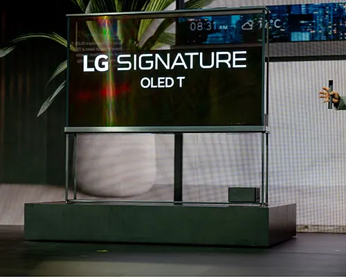TV LG Signature OLED T su base verde scuro. Lo schermo mostra "LG SIGNATURE OLED T". Sullo schermo appaiono ora e temperatura.