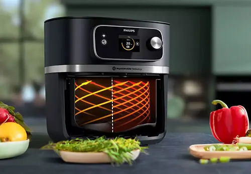 Una friggitrice ad aria nera con un display digitale � su un bancone vicino a verdure fresche.