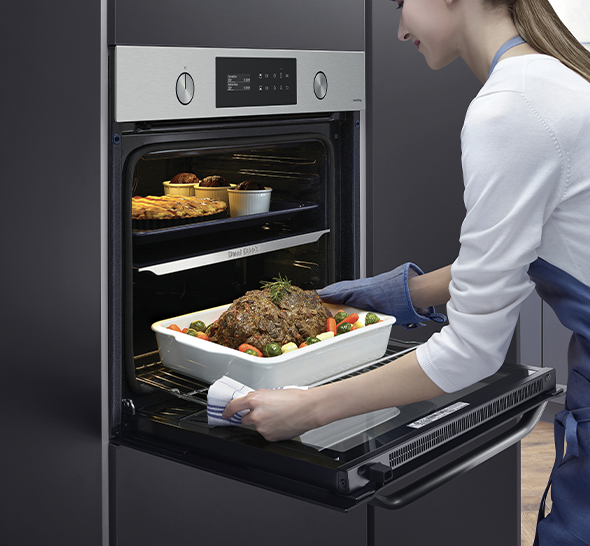 Donna che usa un forno nero integrato con arrosto e contorni nel piatto bianco. Altri cibi cotti sullo scaffale.