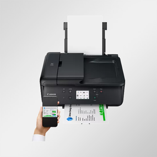 Stampante nera con carta, in funzione. Uno smartphone mostra grafici verdi. Una mano tiene il telefono. Lo sfondo � bianco.