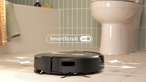 Aspirapolvere robot nero su piastrelle chiare in bagno. Dietro, un water bianco e una parete con piastrelle verticali chiare.