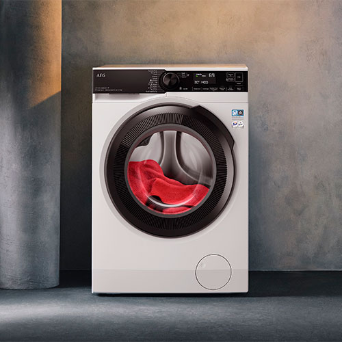 Lavatrice bianca con obl� nero, indumenti rossi all'interno. Pannello comandi nero in alto, su sfondo grigio.