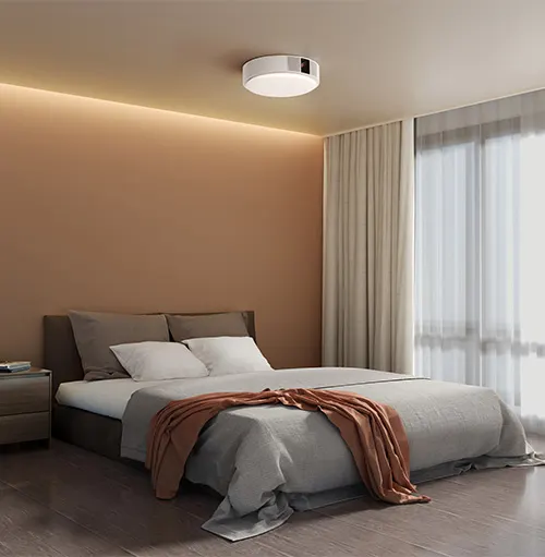 Camera da letto con letto matrimoniale, comodino e lampada a soffitto bianca. Tende chiare coprono una finestra.