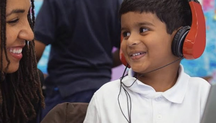 Ragazzo sorridente con cuffie rosse e camicia bianca, interagisce con una donna sorridente in un ambiente scolastico.