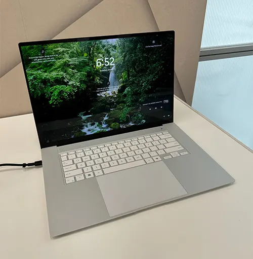 Un computer portatile grigio aperto mostra una cascata sullo schermo. Si vedono una tastiera bianca e un cavo di alimentazione nero.