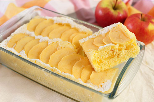 Torta di mele in teglia di vetro con mele rosse sullo sfondo. Una fetta � tagliata.