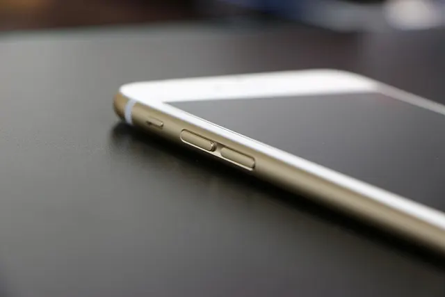 Vista laterale di un telefono bianco e oro su una superficie scura, che mostra i pulsanti del volume.