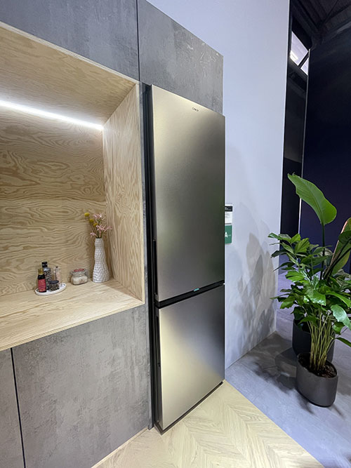 Mobile in cucina con ripiano illuminato, frigorifero in acciaio e pianta verde in vaso.
