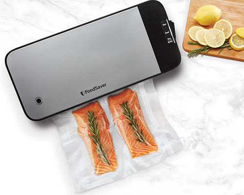 Macchina sottovuoto grigia su confezione con salmone e rosmarino. Tagliere con limoni sullo sfondo.