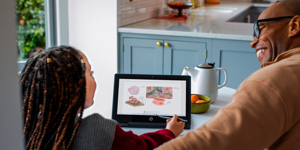 Ragazza e uomo guardano uno schermo. Un laptop mostra illustrazioni mediche. Teiera bianca e arance su un tavolo da cucina.