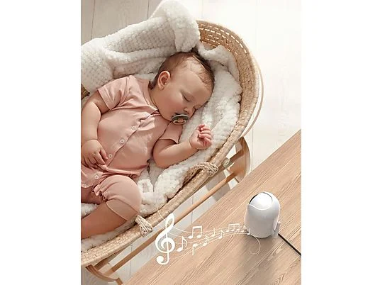 Neonato dorme in culla di vimini con coperta bianca. Un apparecchio bianco è su un tavolo di legno con note musicali.
