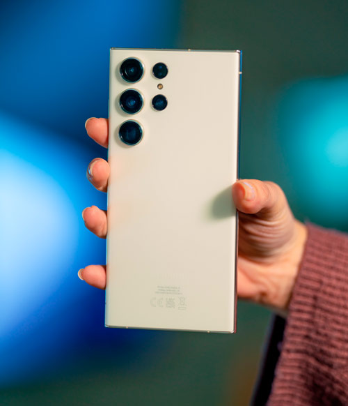 Una mano tiene un telefono con diverse lenti su uno sfondo blu.