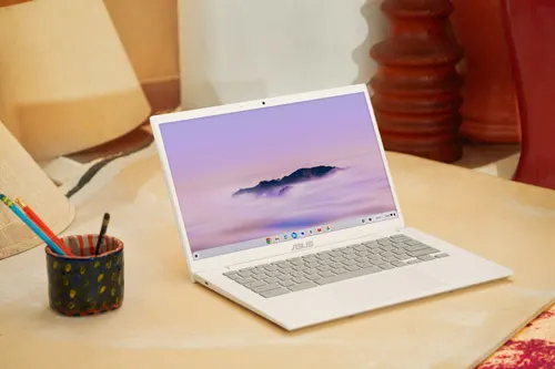 Laptop bianco aperto su un tavolo con portapenne e cuscini sullo sfondo. Lo schermo mostra un paesaggio.