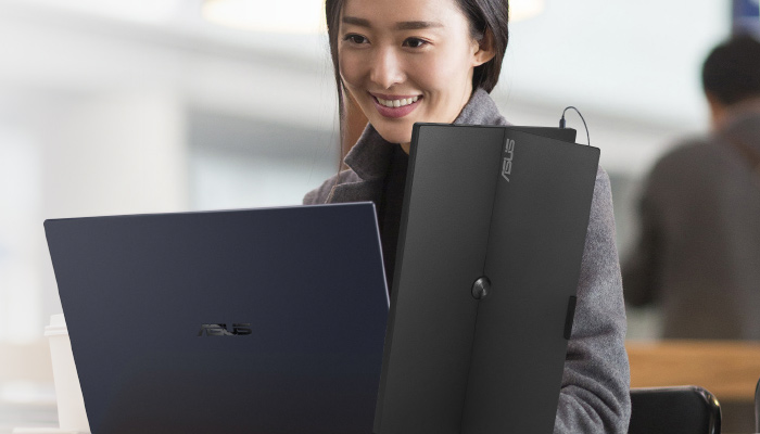 Donna sorridente con portatile aperto e monitor portatile Asus nero. Ufficio luminoso sullo sfondo.